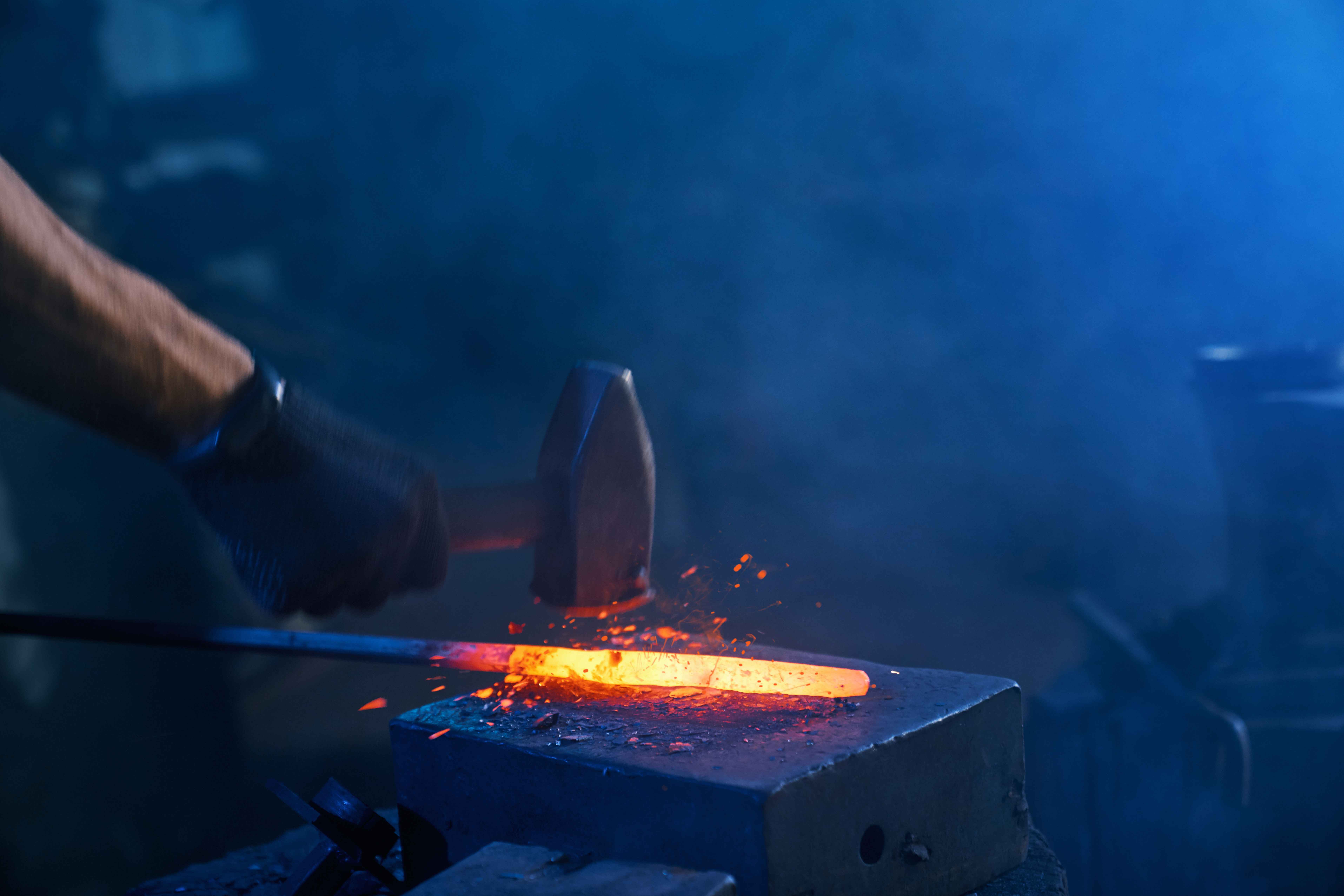 close up strong male hands forging molten metal