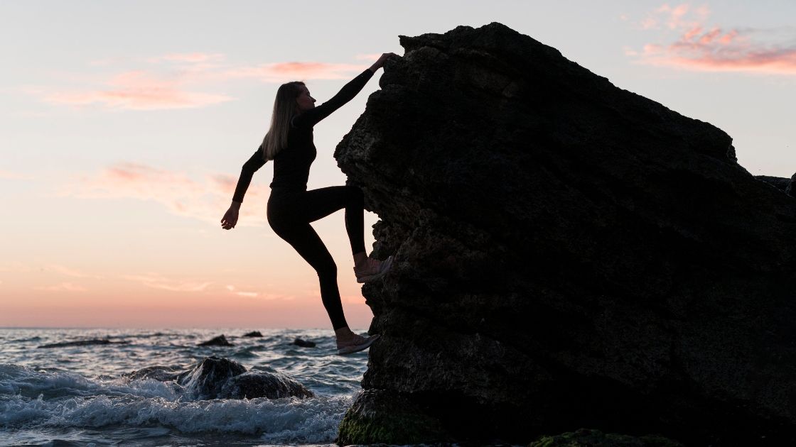 woman climbing the rock next to the ocean displaying resilience