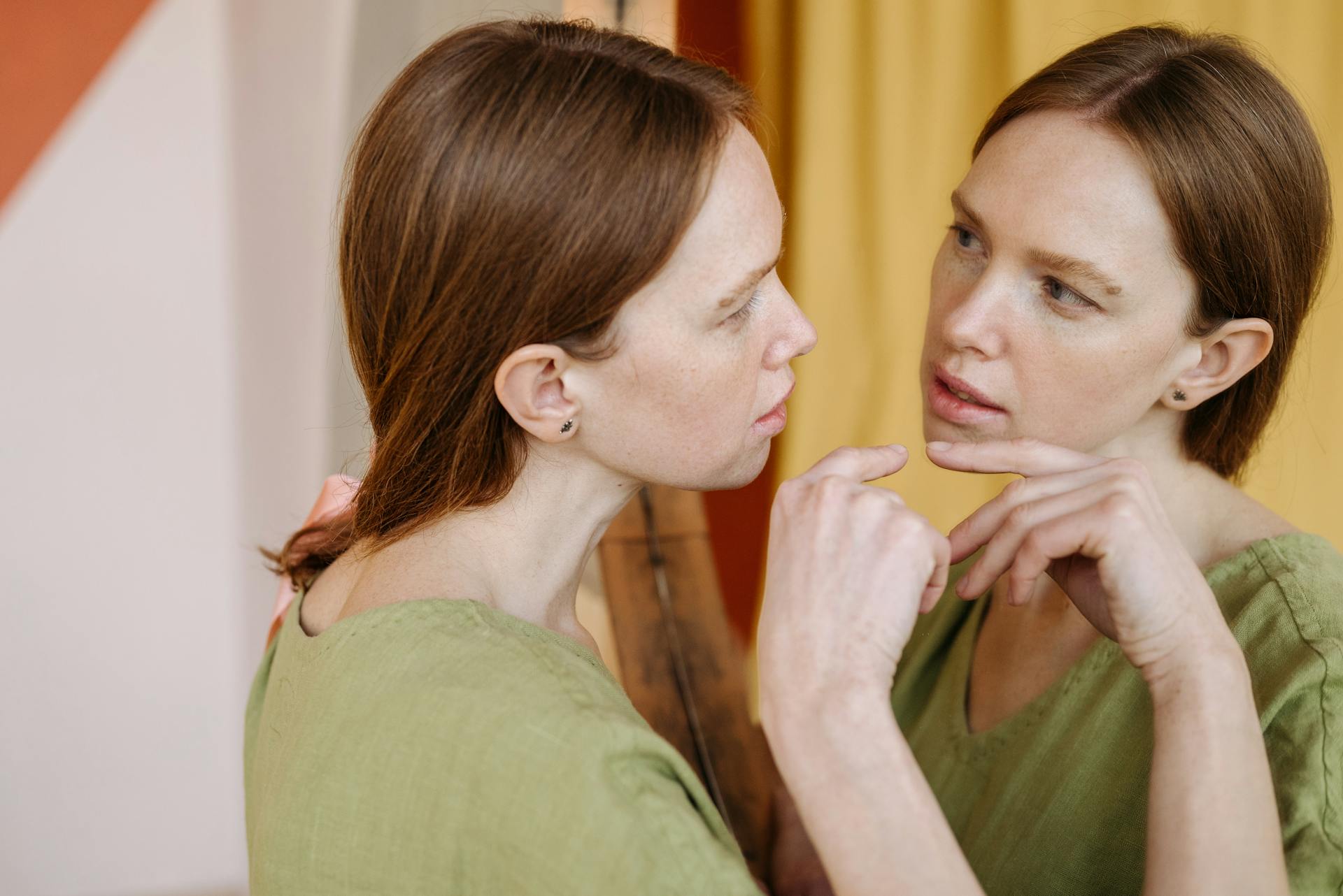 a woman gazes thoughtfully into a mirror