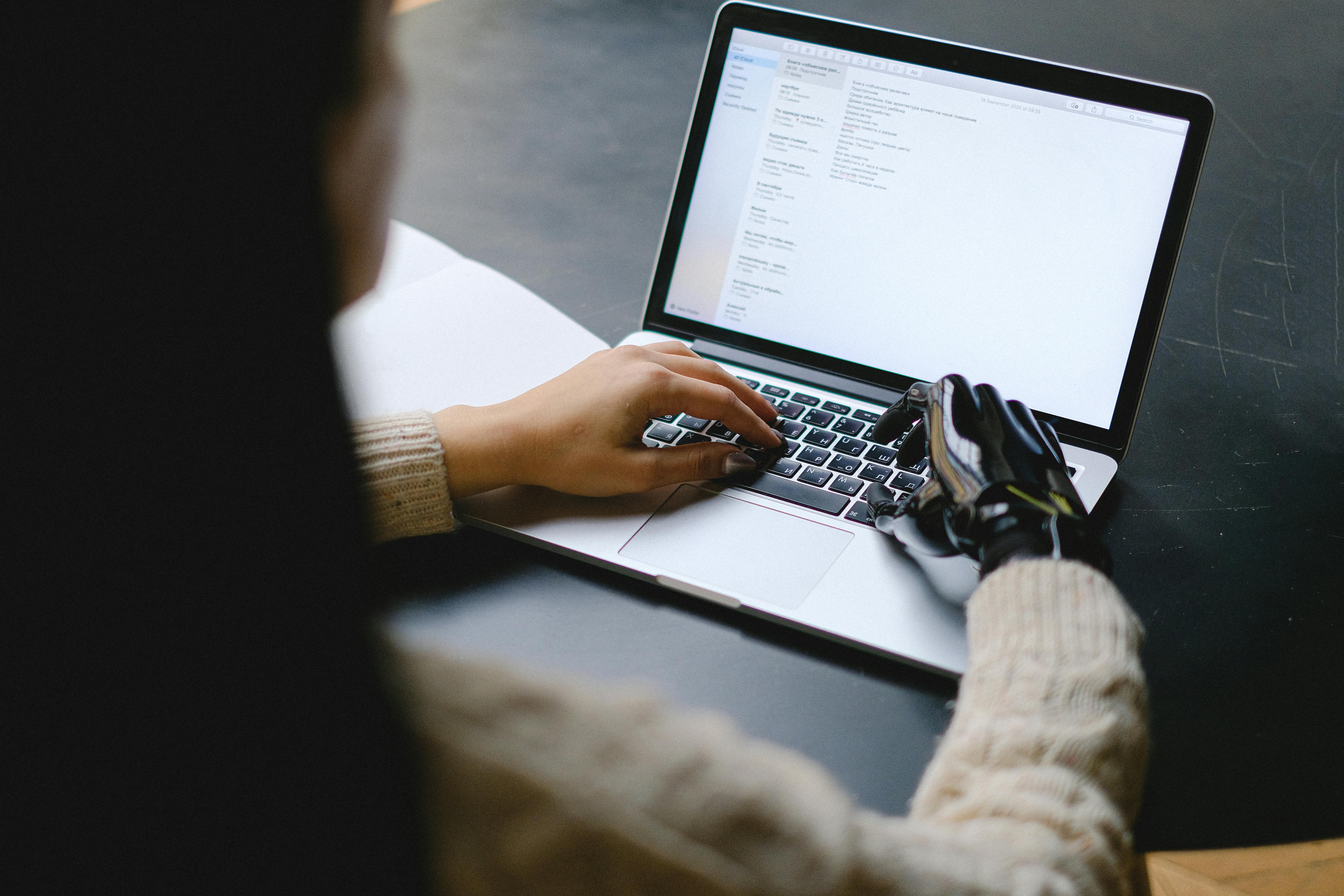 Seseorang dengan Tangan Prostetik Sedang Mengetik di Laptop