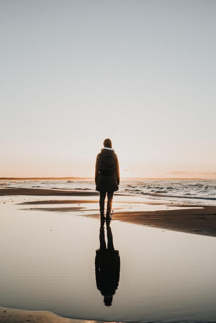 woman in coat standing on beach with reflection