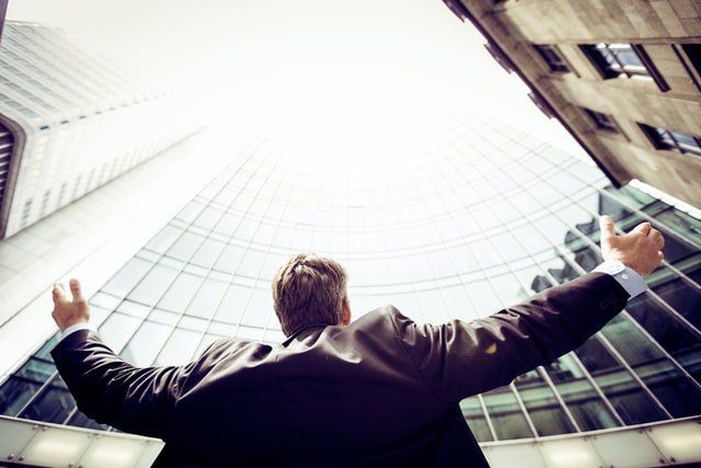 C-Level Leader looking up a building with his hands up